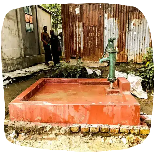 Pompe à eau manuelle installée sur une plateforme en béton dans un village bangladais, offrant un accès à l'eau potable.