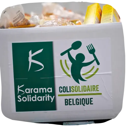 Karama Solidarity logosu ve 'Colis Solidaire Belgique' etiketiyle, zor durumdaki aileler için yiyeceklerle dolu bir gıda paketi.