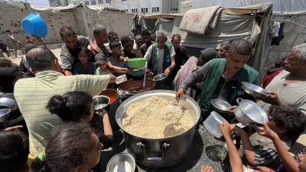 Des bénévoles distribuent des plats de riz chaud à une foule de familles et d'enfants rassemblés autour d'un grand chaudron dans un camp de réfugiés.