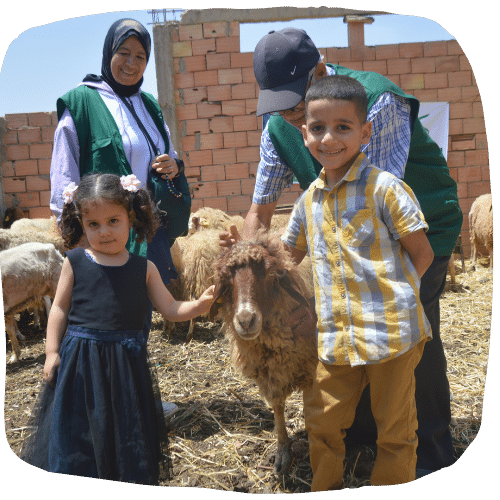 Deux enfants souriants caressant un mouton entourés de volontaires de Karama Solidarity.
