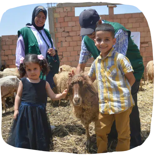 Twee glimlachende kinderen die een schaap aaien, omringd door vrijwilligers van Karama Solidarity.
