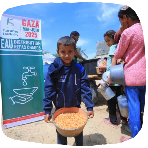 Jeune garçon tenant un bol rempli de pâtes lors d’une distribution de repas chauds à Gaza, avec une banderole de Karama Solidarity visible en arrière-plan.