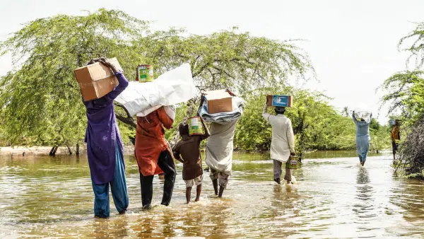 Familles pakistanaises portant des colis d’aide humanitaire de Karama Solidarity à travers une zone inondée en 2025